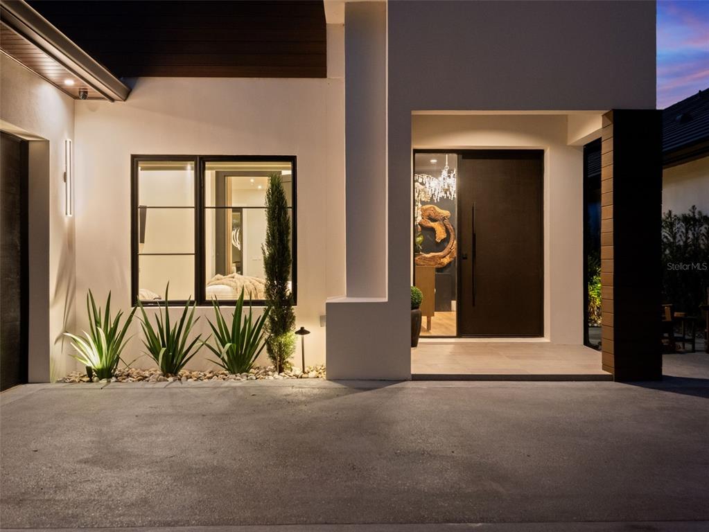 A modern home exterior features a dark front door, large windows, and landscaped desert plants — 10220 CHILTERN GARDEN DRIVE, ORLANDO, FL