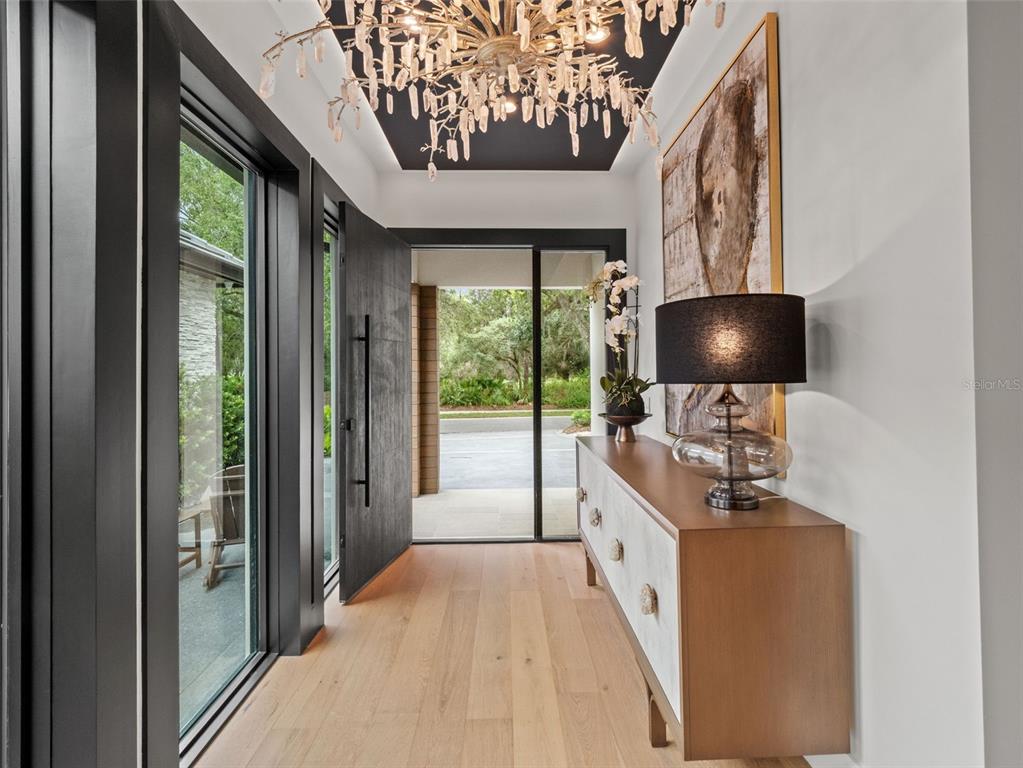 An entryway features light wood flooring, a black ceiling, a crystal chandelier, and a console table — 10220 CHILTERN GARDEN DRIVE, ORLANDO, FL