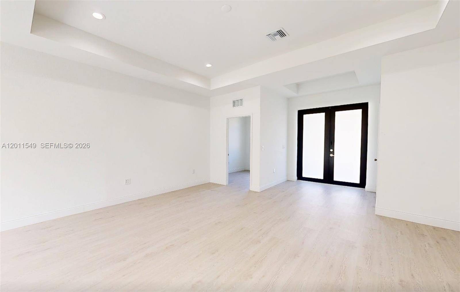 A bright, empty room features white walls, light wood-look flooring, a tray ceiling, and black-framed double doors — 618 SHELDON AVE, Lehigh Acres FL 33936, LEHIGH ACRES, FL