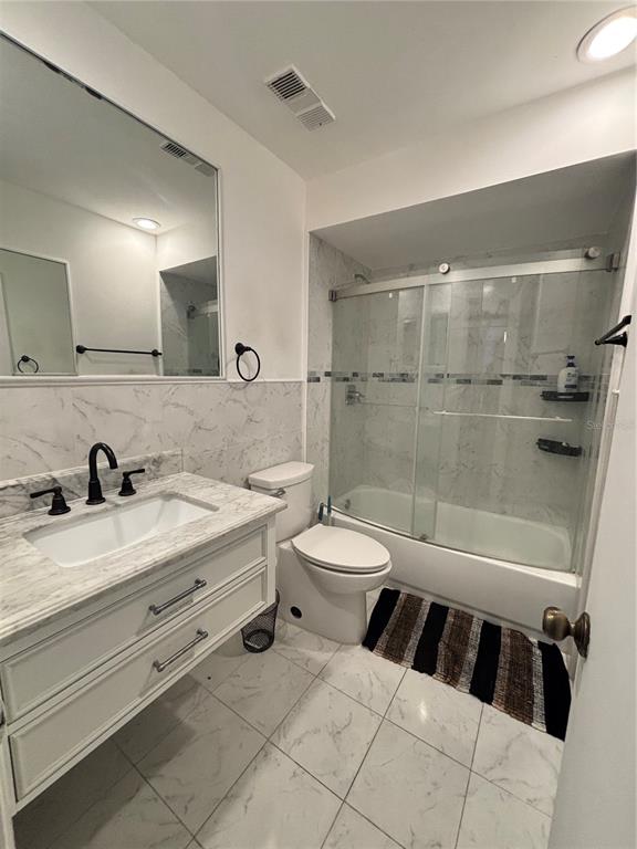 A bathroom features a marble-topped vanity, a toilet, and a shower-tub combination with glass doors — 2487 HARBOUR WAY, WINTER PARK, FL