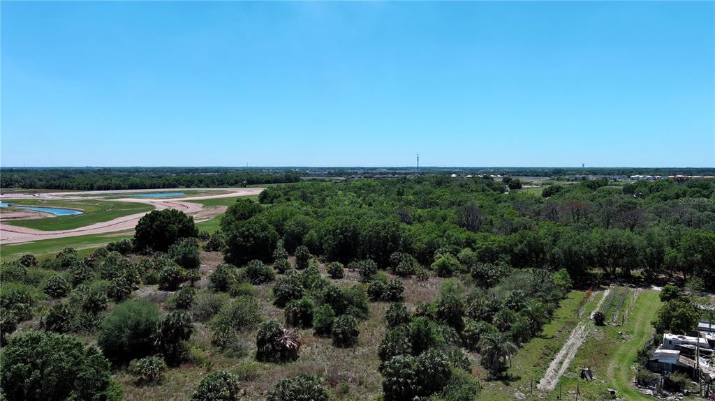 An aerial view shows a large, undeveloped plot of land with trees and nearby construction — 12870 GRASS FARM ROAD, PALMETTO, FL