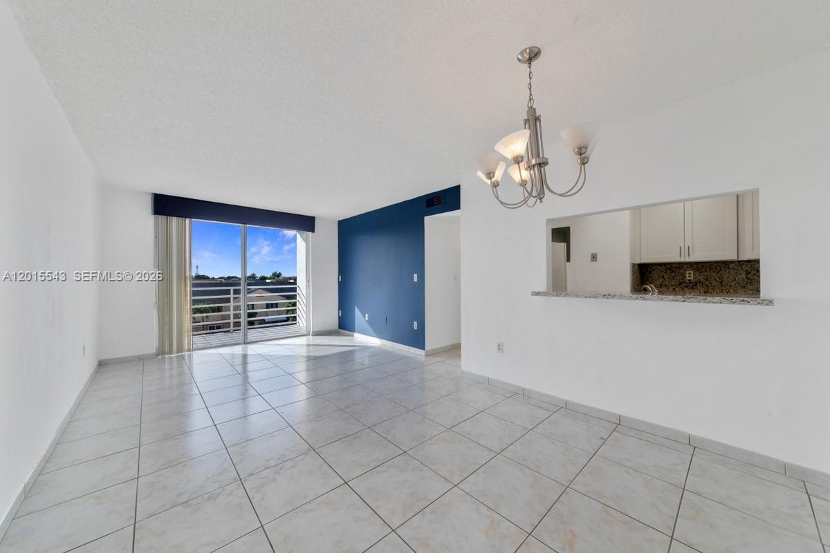 An empty room features white tile floors, a blue accent wall, and a kitchen pass-through — 11715 SW 18th St # 410, Miami FL 33175, MIAMI, FL