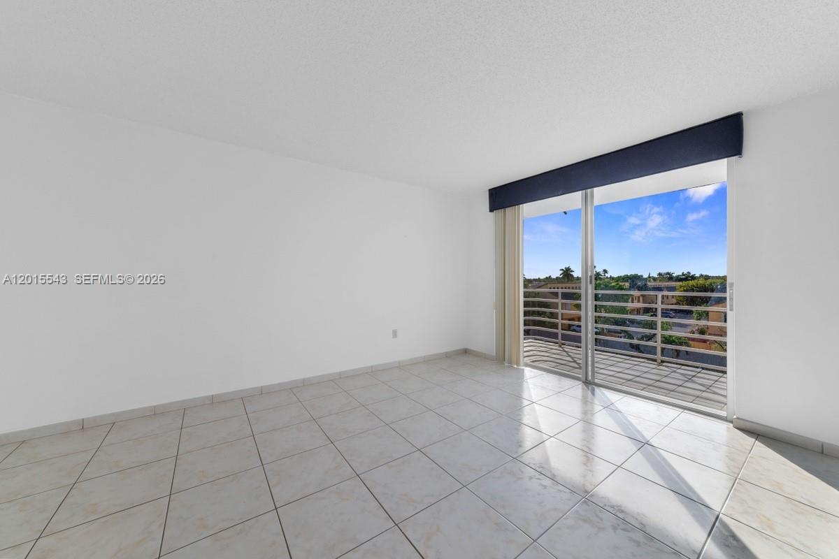 An empty room features white tile flooring, plain white walls, and a sliding glass door — 11715 SW 18th St # 410, Miami FL 33175, MIAMI, FL