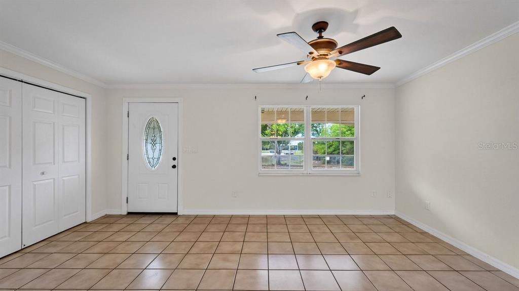 An empty room features beige tile flooring, a ceiling fan, a white door, and windows — 2791 FULFORD STREET, DELTONA, FL