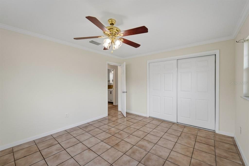 An empty bedroom features tan tile flooring, a ceiling fan, and white sliding closet doors — 2791 FULFORD STREET, DELTONA, FL
