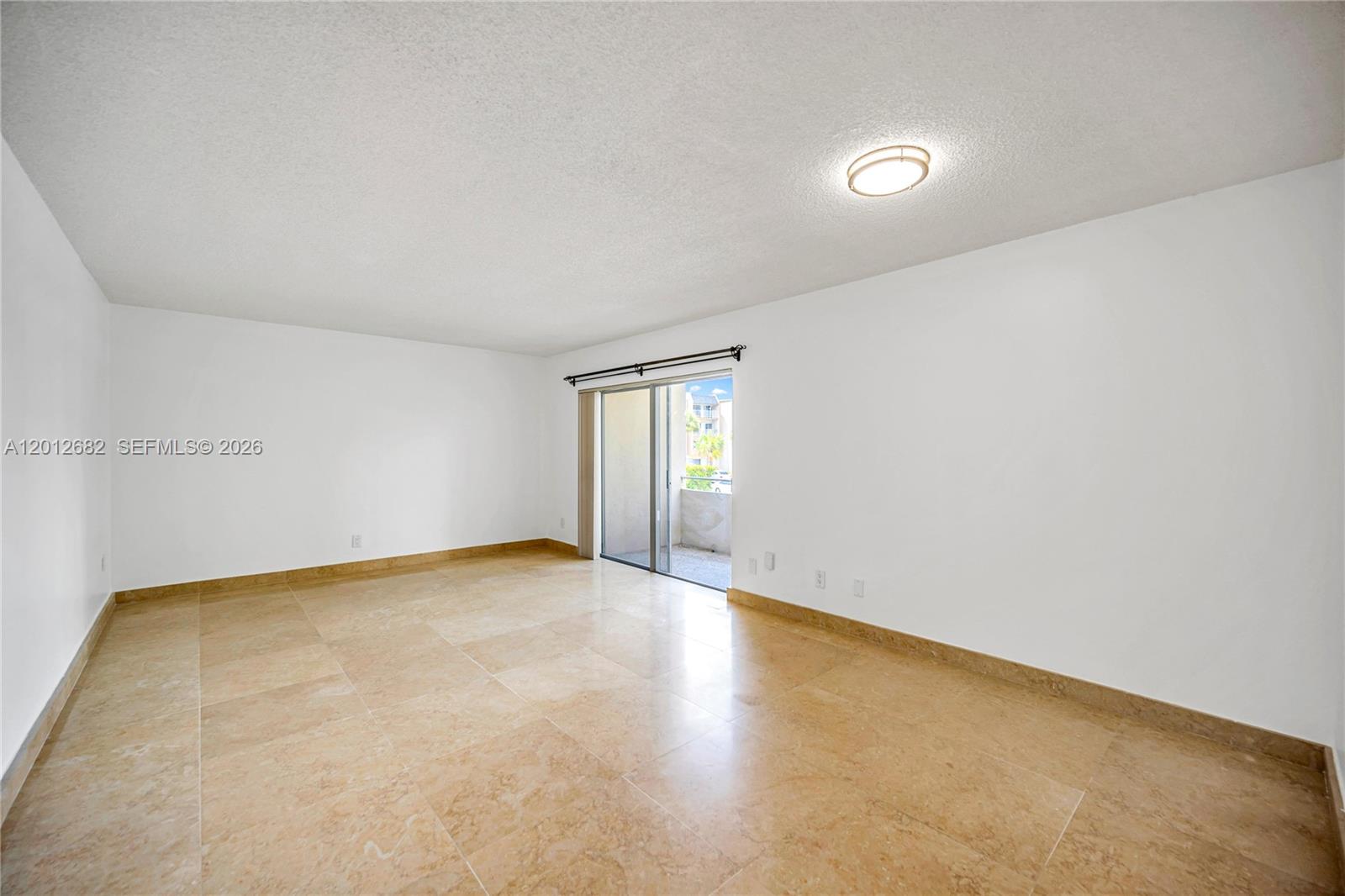 An empty room features beige tile flooring, white walls, and a sliding glass balcony door — 7757 SW 86th St # 213, Miami FL 33143, MIAMI, FL
