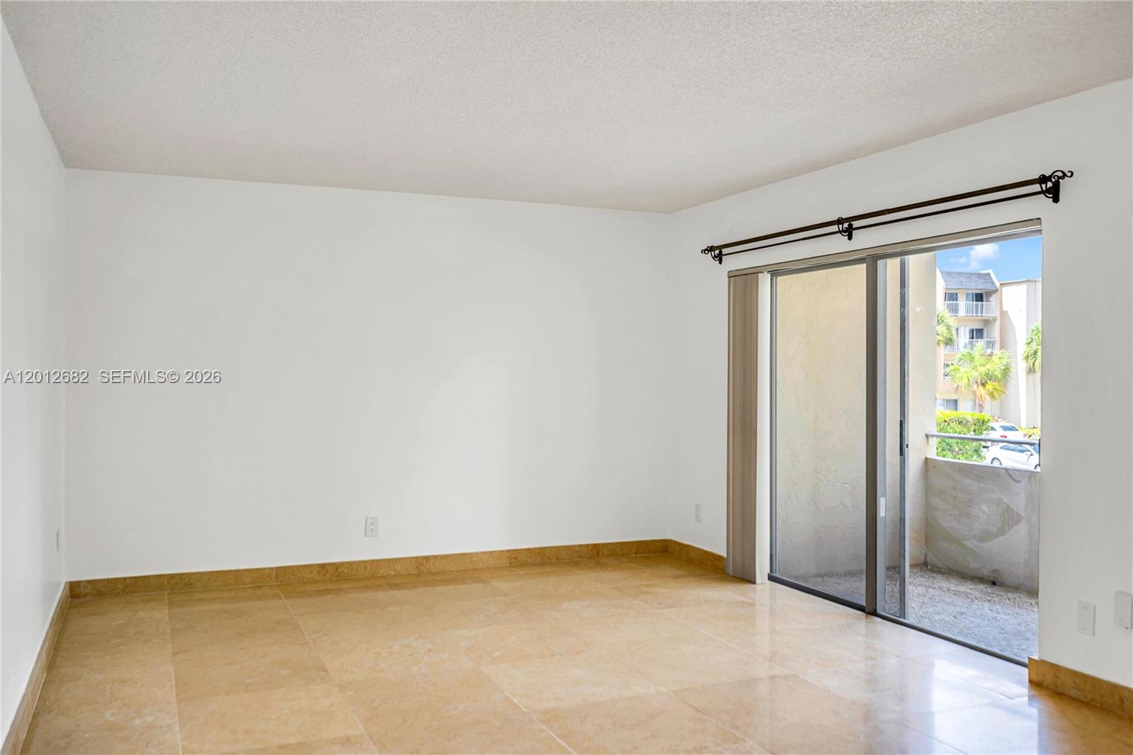 An empty room features beige tile flooring, white walls, and a sliding glass door — 7757 SW 86th St # 213, Miami FL 33143, MIAMI, FL