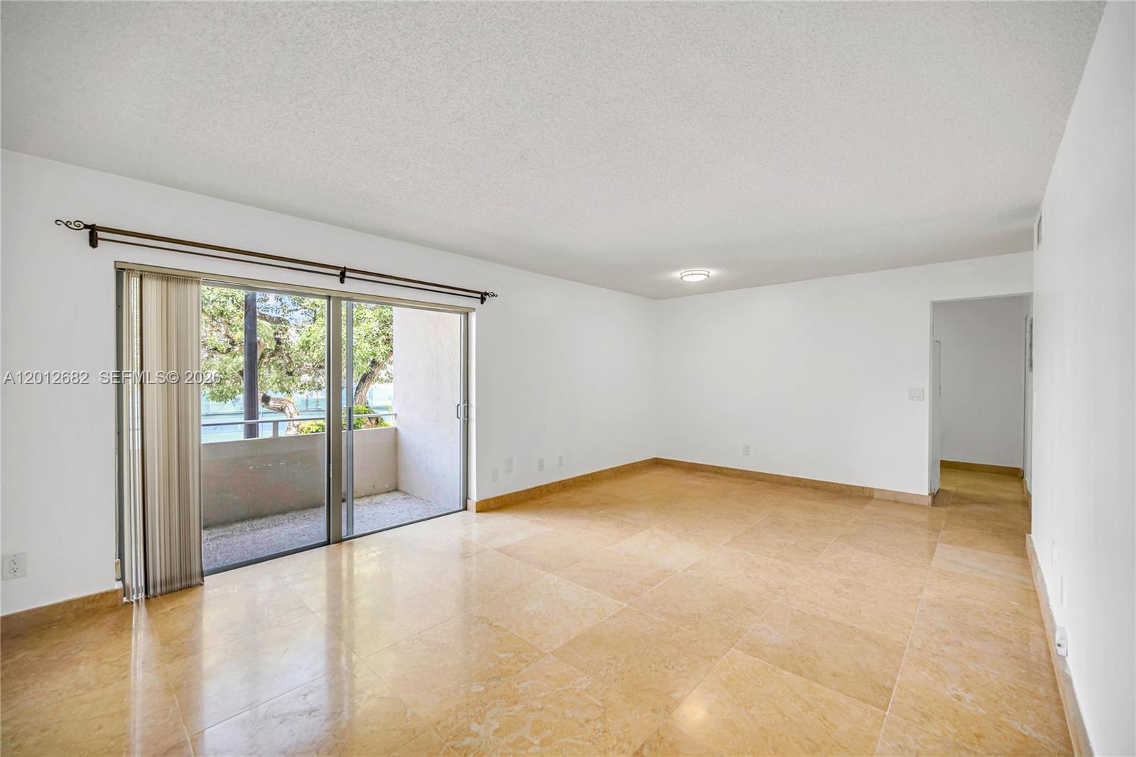 An empty living room features beige tile flooring, white walls, and a sliding glass balcony door — 7757 SW 86th St # 213, Miami FL 33143, MIAMI, FL