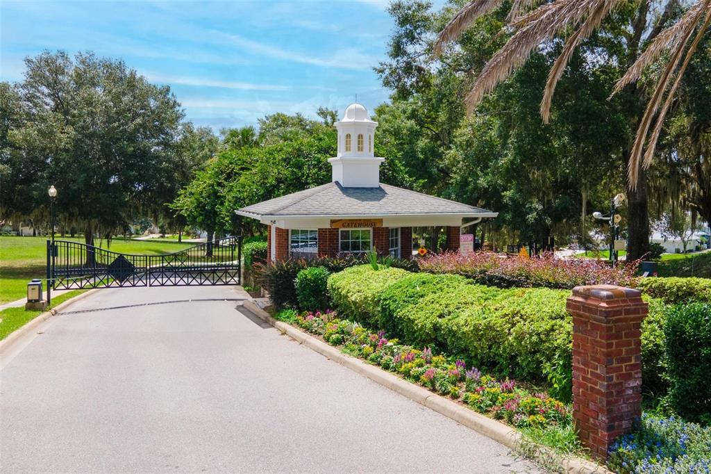 A brick gatehouse with a white cupola stands beside a gated entrance and landscaped gardens — 6115 LANDINGS BOULEVARD, LADY LAKE, FL