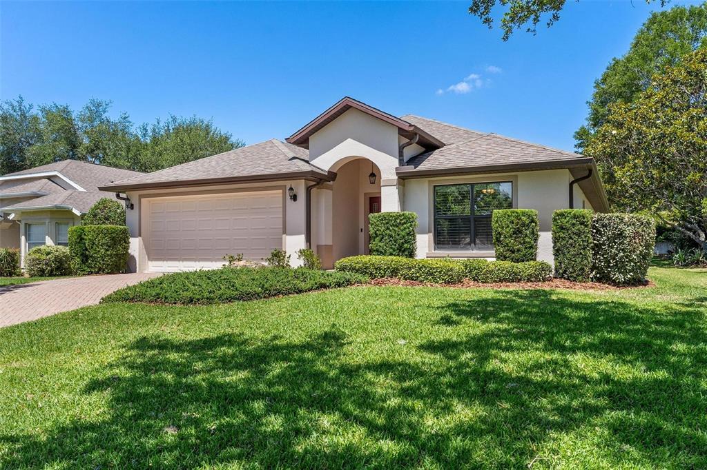 A single-story house with a beige stucco exterior, a two-car garage, and a landscaped lawn — 6115 LANDINGS BOULEVARD, LADY LAKE, FL