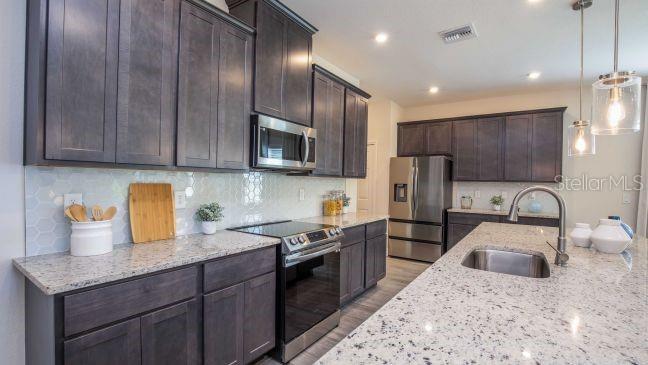 A modern kitchen features dark wood cabinetry, granite countertops, stainless steel appliances, and a central island — 31530 WILD GRAPE LANE, BROOKSVILLE, FL