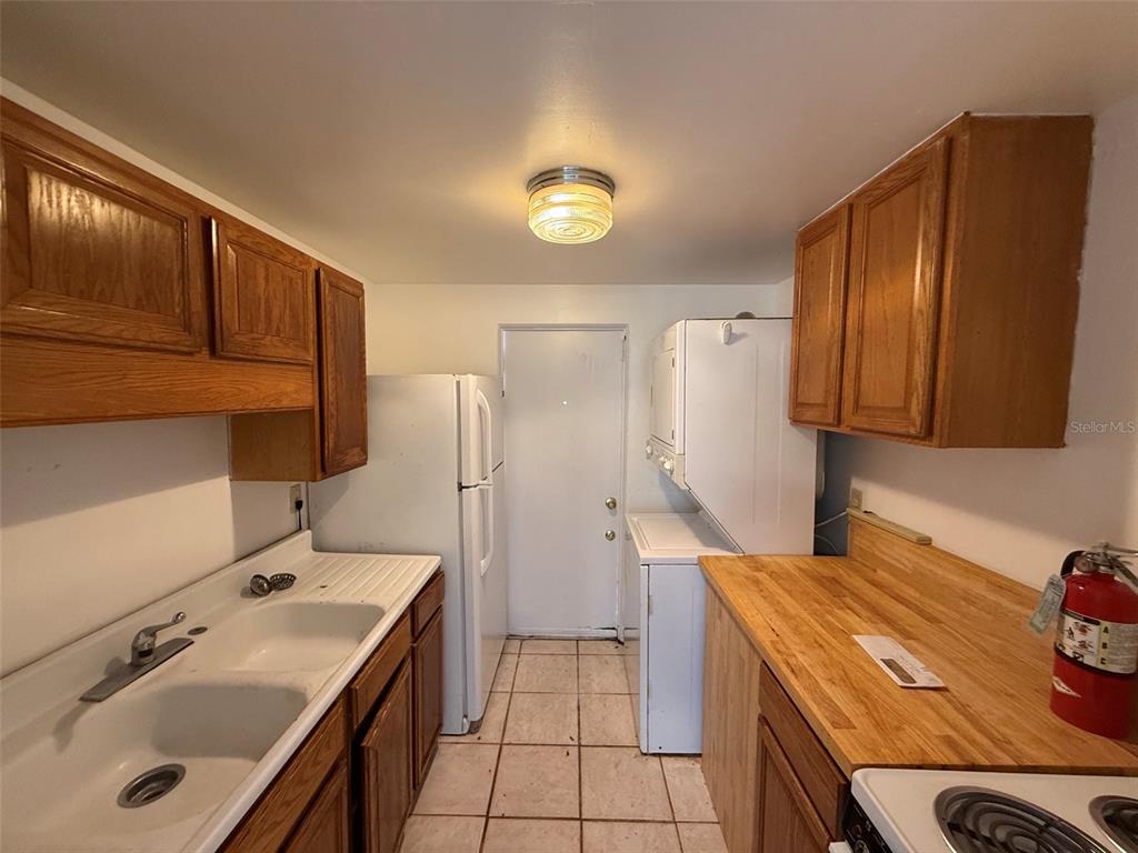 A kitchen features wood cabinets, a white sink, a refrigerator, and a stacked laundry unit — 912 SW 6TH AVENUE, GAINESVILLE, FL