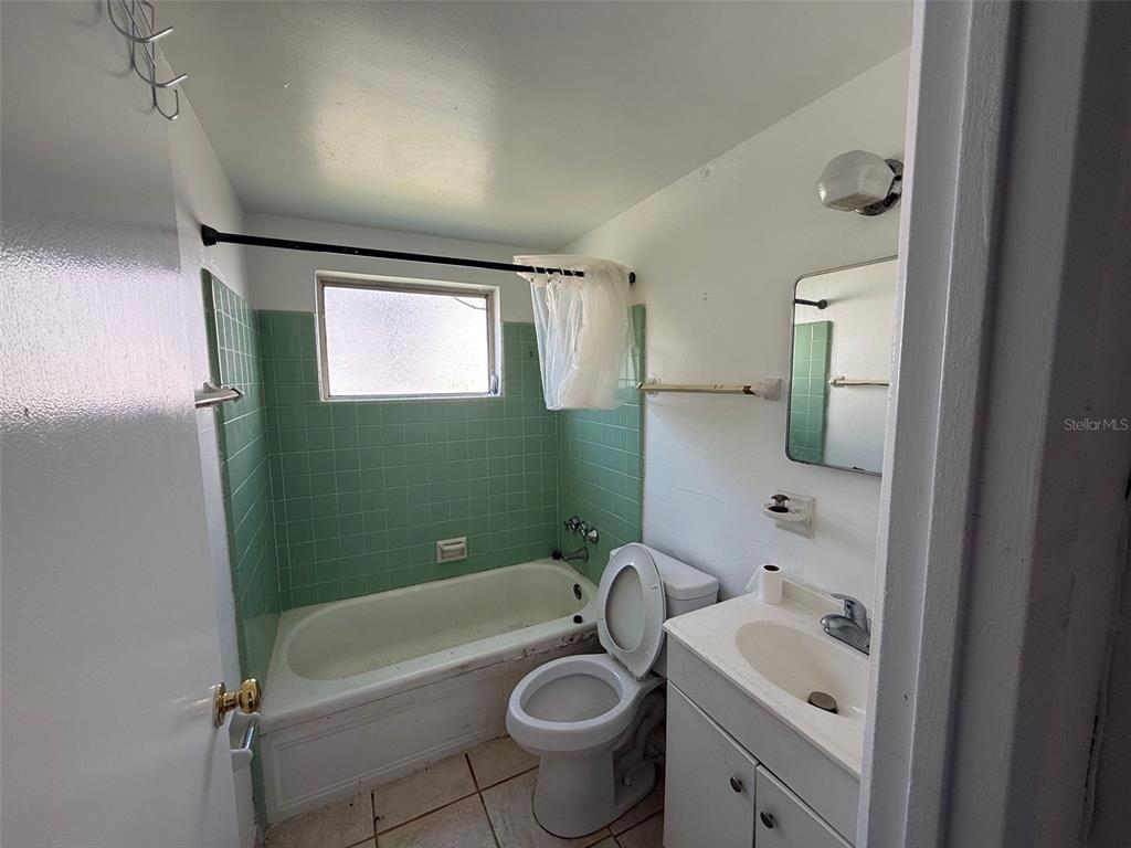 A bathroom features a green-tiled tub surround, a white vanity, and a toilet — 912 SW 6TH AVENUE, GAINESVILLE, FL