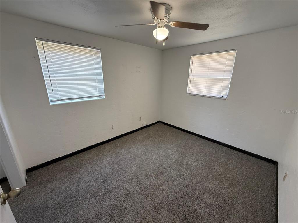 An empty bedroom features white walls, gray carpeting, two windows with blinds, and a ceiling fan — 912 SW 6TH AVENUE, GAINESVILLE, FL