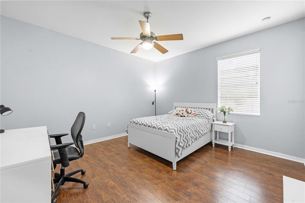 A bedroom features light gray walls, wood-look flooring, a white bed, and a desk — 3540 MOONDANCE CIRCLE, BROOKSVILLE, FL