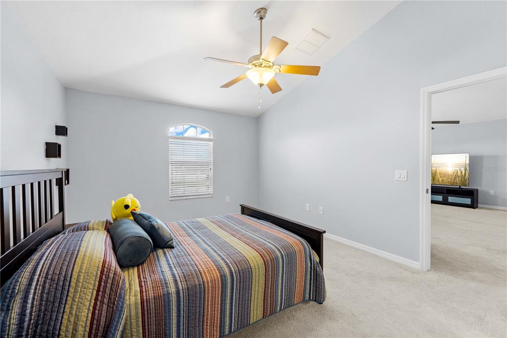 A bedroom features a bed with a striped quilt, a ceiling fan, and a doorway — 3540 MOONDANCE CIRCLE, BROOKSVILLE, FL