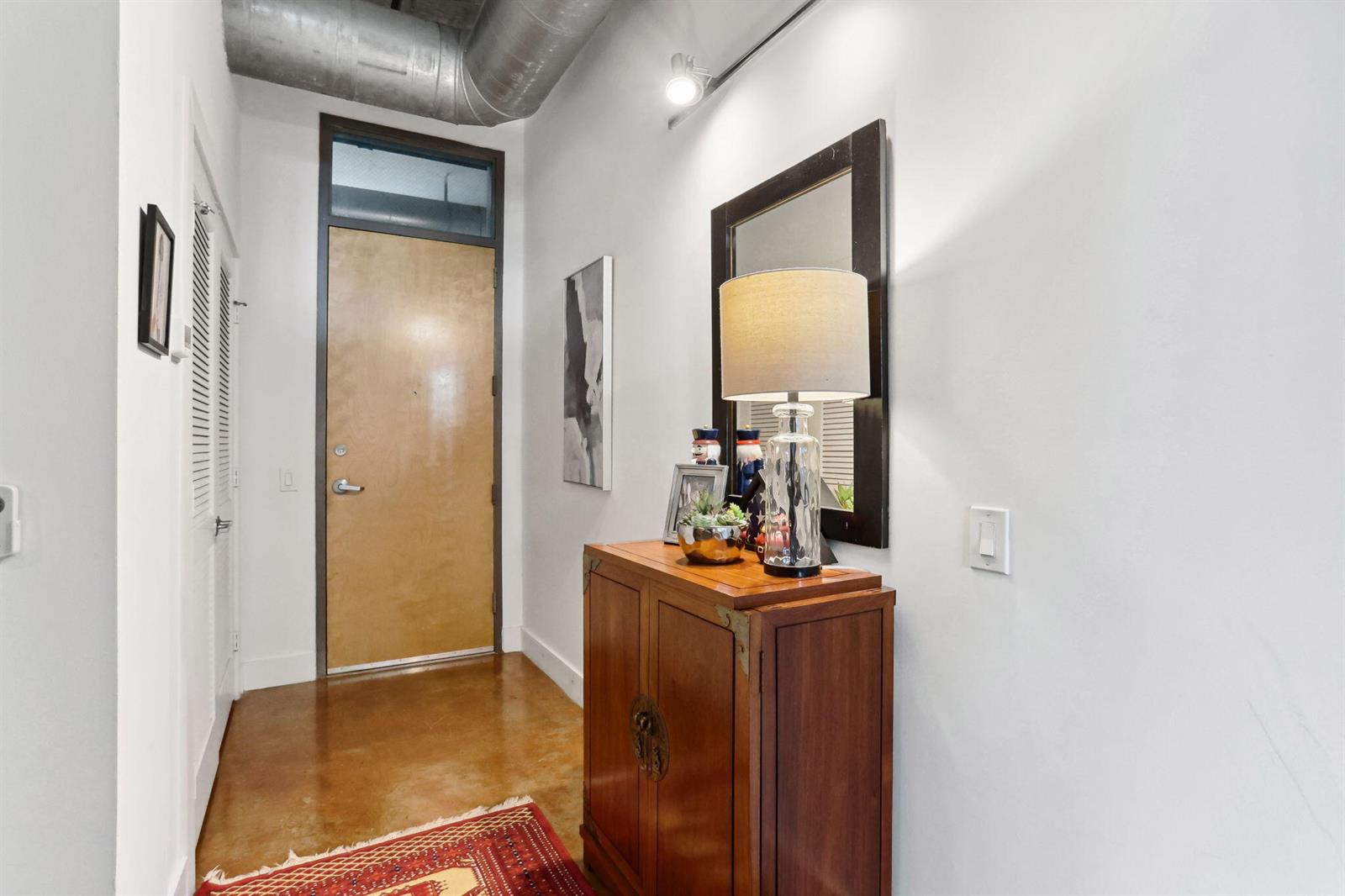 An entryway features a wooden cabinet, a lamp, a mirror, and a concrete floor — 180 NE 4th Avenue # 307, Delray Beach FL 33483, DELRAY BEACH, FL