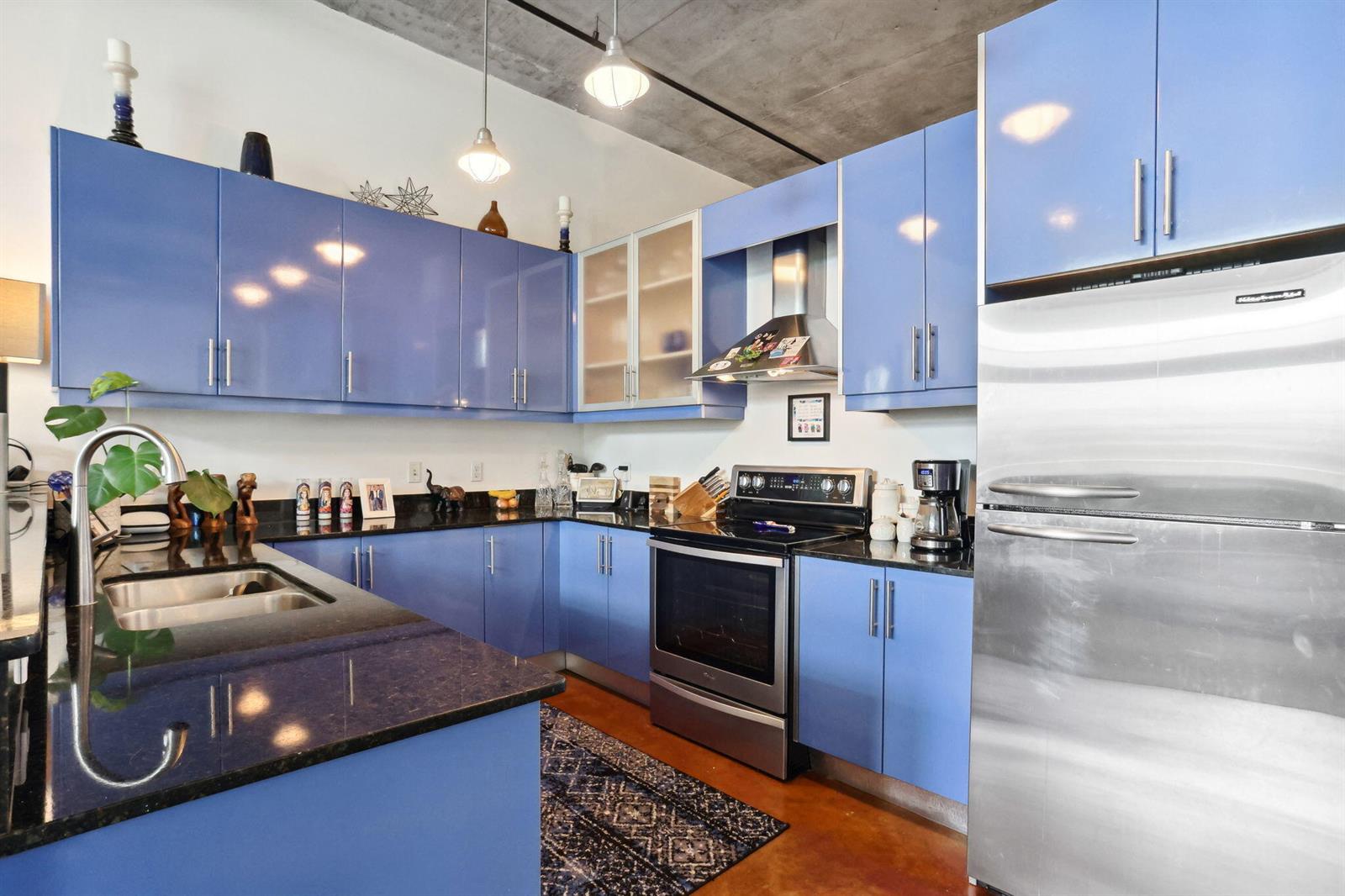 A kitchen features blue cabinets, black countertops, stainless steel appliances, and an exposed concrete ceiling — 180 NE 4th Avenue # 307, Delray Beach FL 33483, DELRAY BEACH, FL