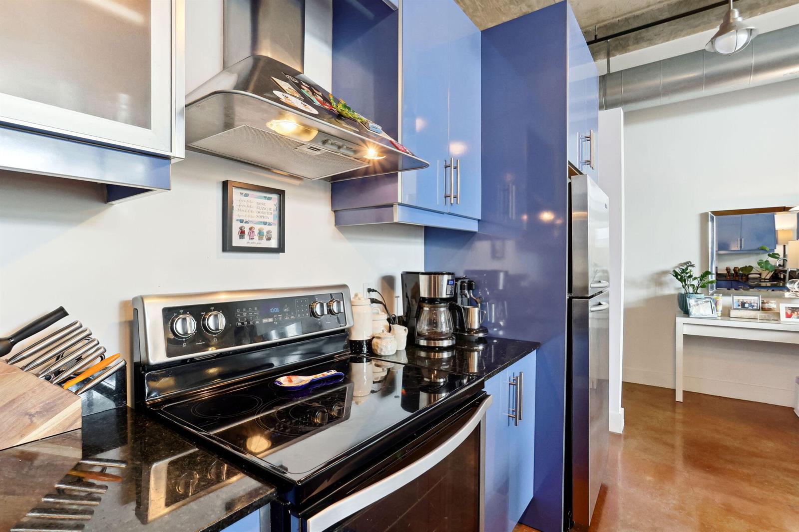 A kitchen features blue cabinets, black countertops, stainless steel appliances, and a concrete ceiling — 180 NE 4th Avenue # 307, Delray Beach FL 33483, DELRAY BEACH, FL