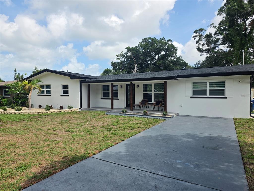 A single-story white house with a black roof, a front porch, and a concrete driveway — 1446 ADMIRAL WOODSON LANE, CLEARWATER, FL