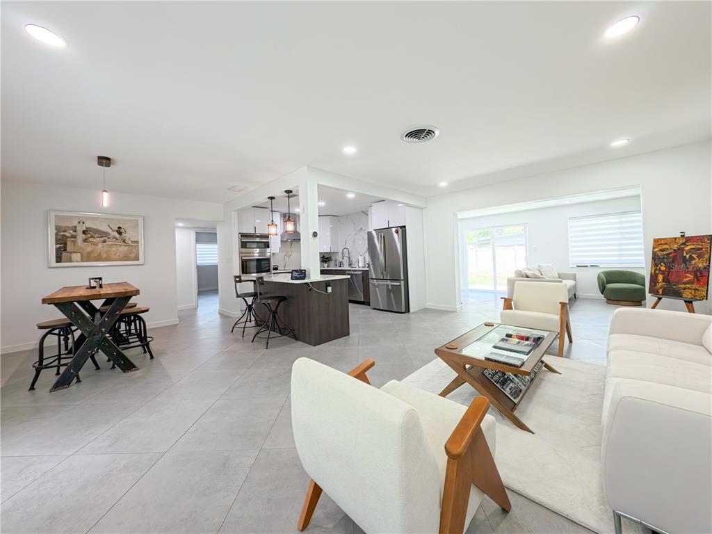 An open-concept living and dining area features tile floors, a modern kitchen, and white furniture — 1446 ADMIRAL WOODSON LANE, CLEARWATER, FL