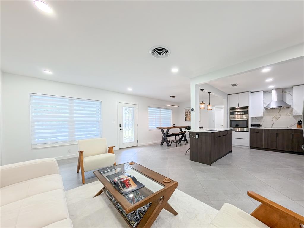 An open-concept living room and kitchen featuring tile floors, white cabinetry, and modern furniture — 1446 ADMIRAL WOODSON LANE, CLEARWATER, FL