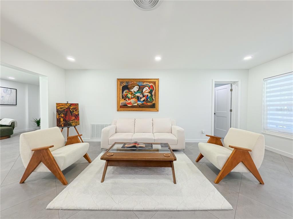 A living room features a white sofa, two wooden armchairs, a coffee table, and artwork — 1446 ADMIRAL WOODSON LANE, CLEARWATER, FL
