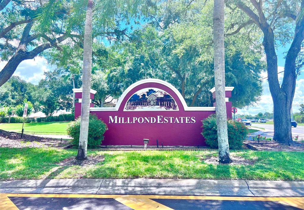 A maroon Millpond Estates community sign stands between two palm trees near a road — 7910 HARDWICK DRIVE UNIT 713, NEW PORT RICHEY, FL