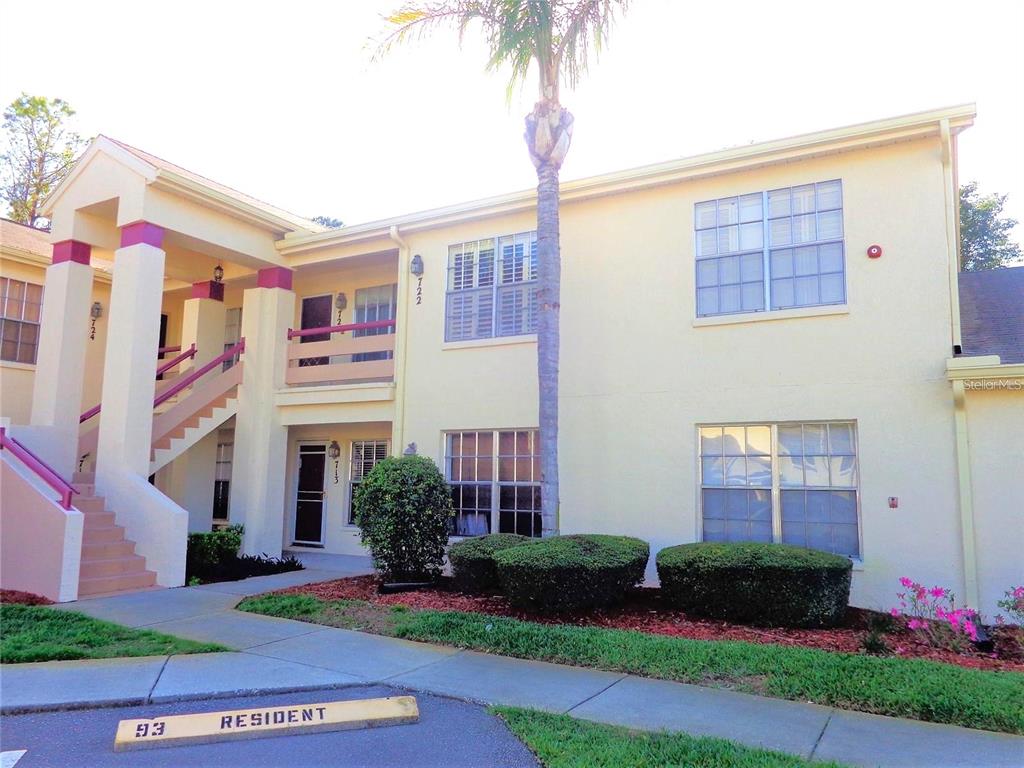 A two-story apartment building with beige stucco walls, a palm tree, and exterior stairs — 7910 HARDWICK DRIVE UNIT 713, NEW PORT RICHEY, FL