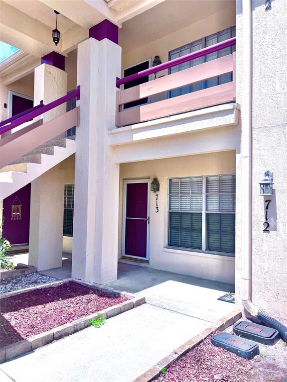 The exterior of a two-story apartment building features purple doors, beige walls, and stairs — 7910 HARDWICK DRIVE UNIT 713, NEW PORT RICHEY, FL