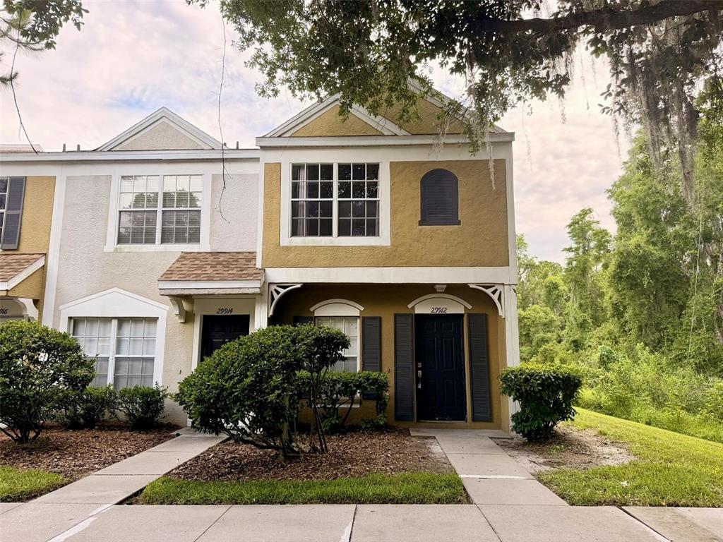 A two-story townhouse exterior with a tan stucco facade, dark doors, and surrounding landscaping — 29912 ALTA VITA LANE, WESLEY CHAPEL, FL