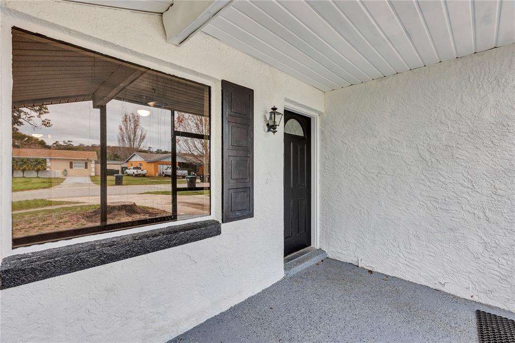 A covered porch features a black front door, a large window, and textured white walls — 7900 TOLEDO STREET, ORLANDO, FL