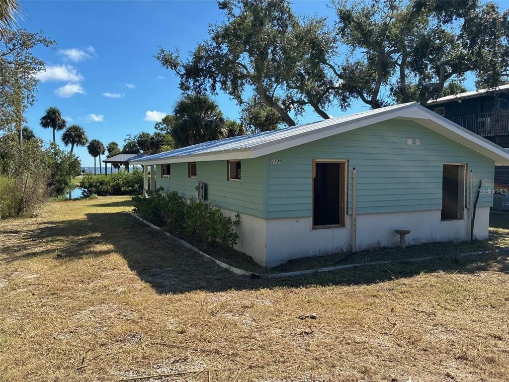 A light green, single-story house with missing windows sits on a grassy lot near water — 1170 WHIDDON AVENUE, CEDAR KEY, FL
