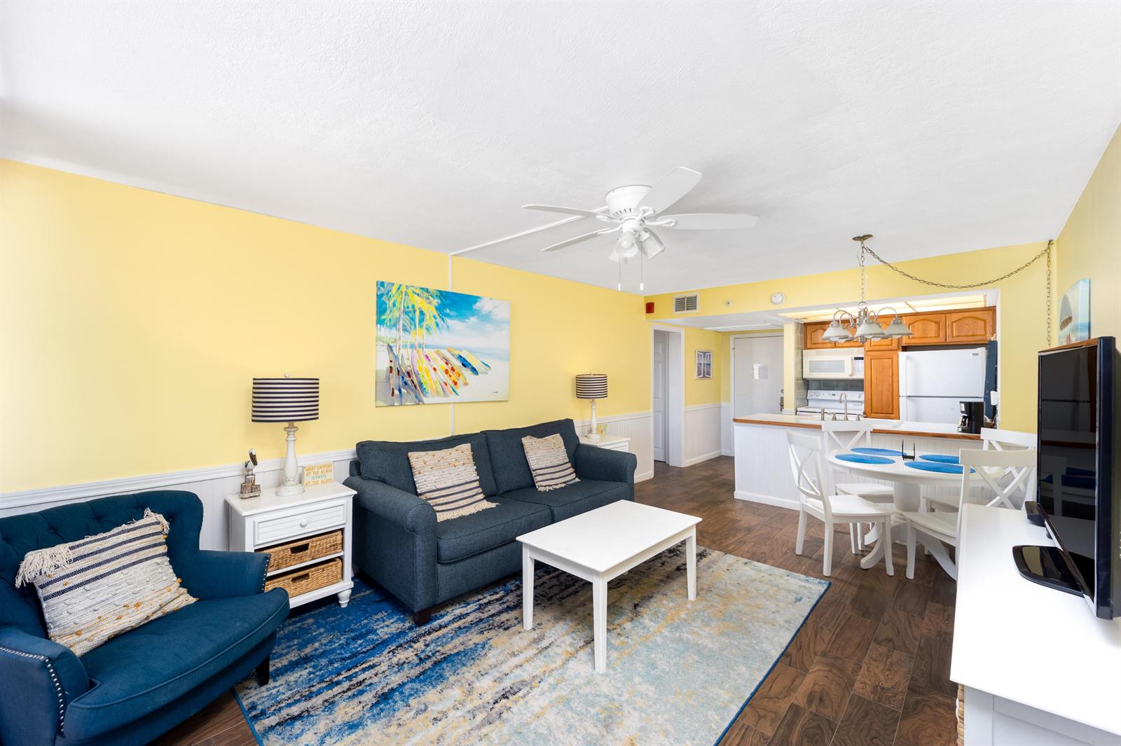A living room with yellow walls, a blue sofa, and an adjacent kitchen with dining area — 9800 S Ocean Drive # 415, Jensen Beach FL 34957, JENSEN BEACH, FL