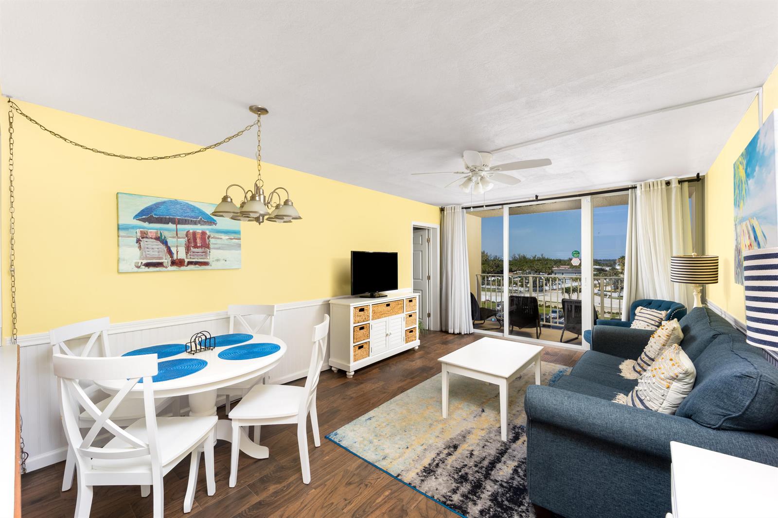 A living and dining area with yellow walls, white furniture, and a balcony view — 9800 S Ocean Drive # 415, Jensen Beach FL 34957, JENSEN BEACH, FL