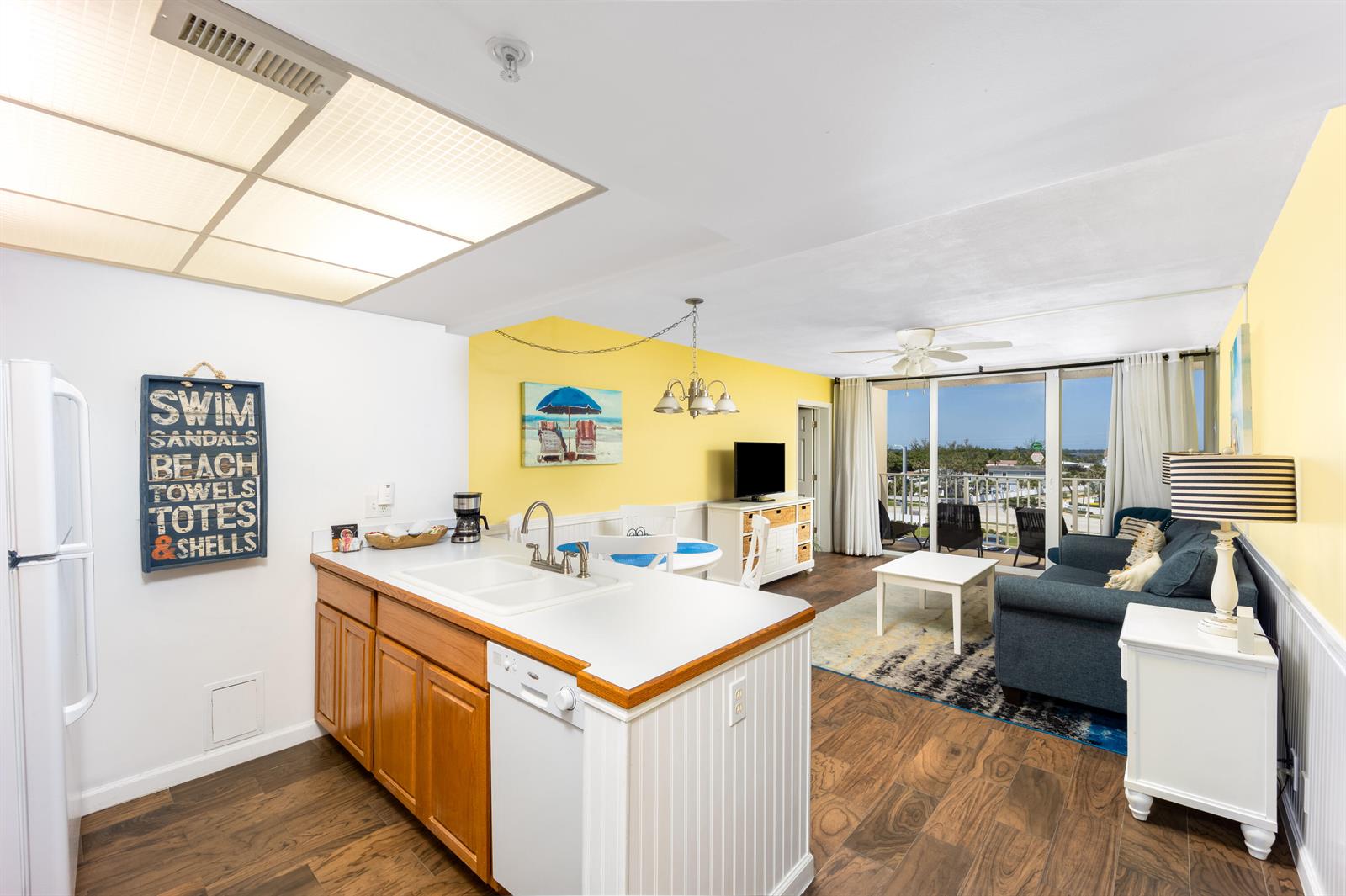 An open-concept kitchen and living area features wood flooring, yellow walls, and a balcony view — 9800 S Ocean Drive # 415, Jensen Beach FL 34957, JENSEN BEACH, FL