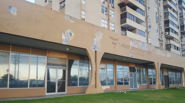 A low-rise commercial building with arched supports sits in front of a tall apartment complex — PR 190 int PONTEZUELA AVENUE, CAROLINA, PR