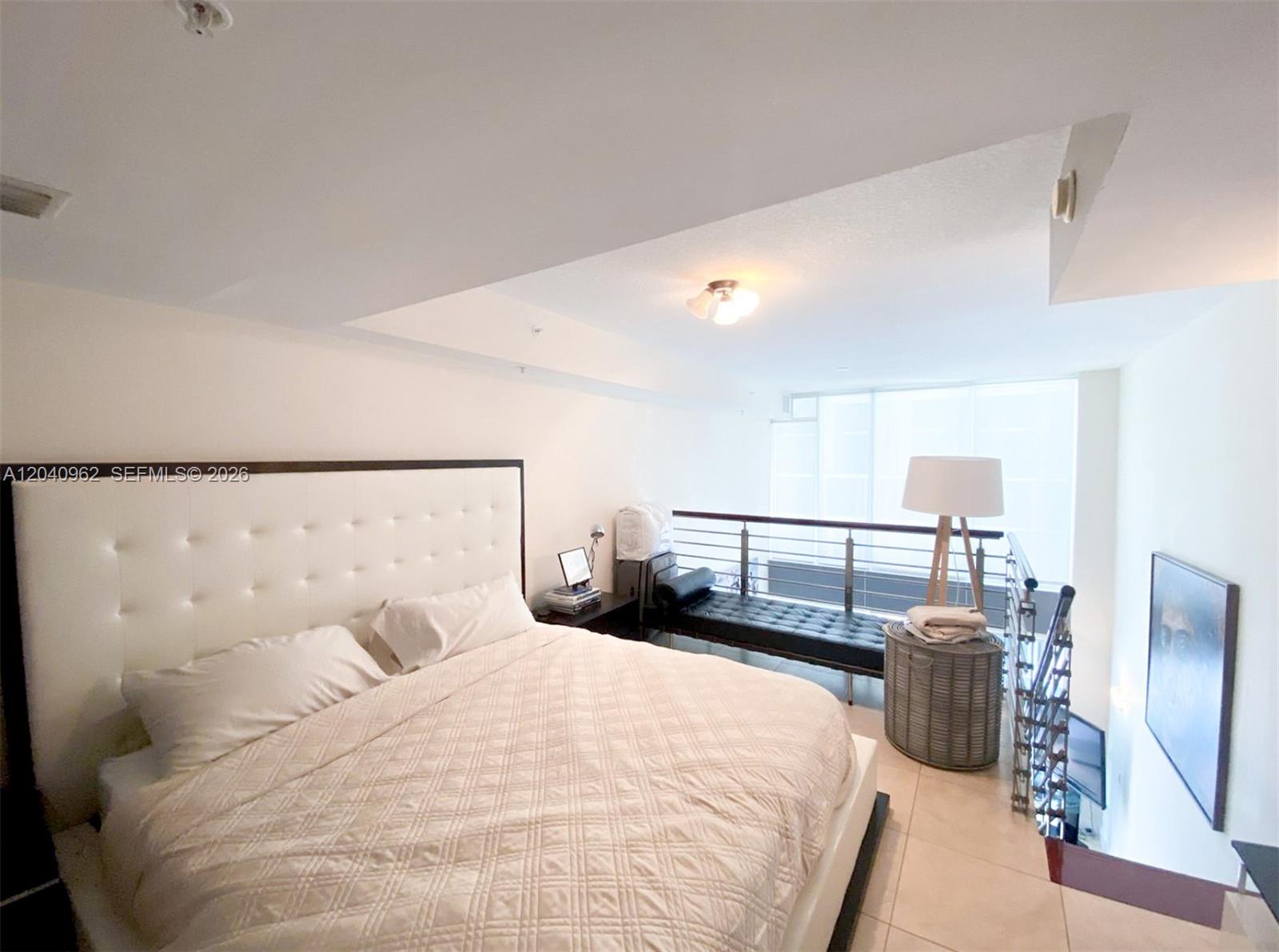 A bedroom with a tufted headboard overlooks a lower level via a metal railing — 41 SE 5th St # 1006, Miami FL 33131, MIAMI, FL