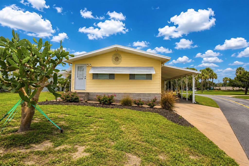 A yellow single-story house with a carport, metal awnings, and a large cactus in the yard — 4234 ROLLING OAKS DRIVE, WINTER HAVEN, FL
