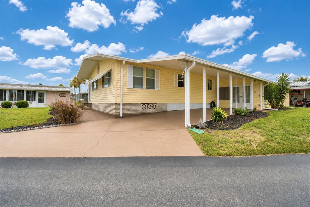 A yellow mobile home with a carport and a concrete driveway under a blue sky — 4234 ROLLING OAKS DRIVE, WINTER HAVEN, FL