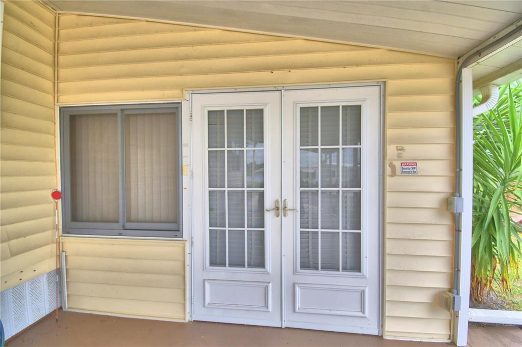 A covered porch features yellow vinyl siding, a sliding window, and white French doors — 4234 ROLLING OAKS DRIVE, WINTER HAVEN, FL