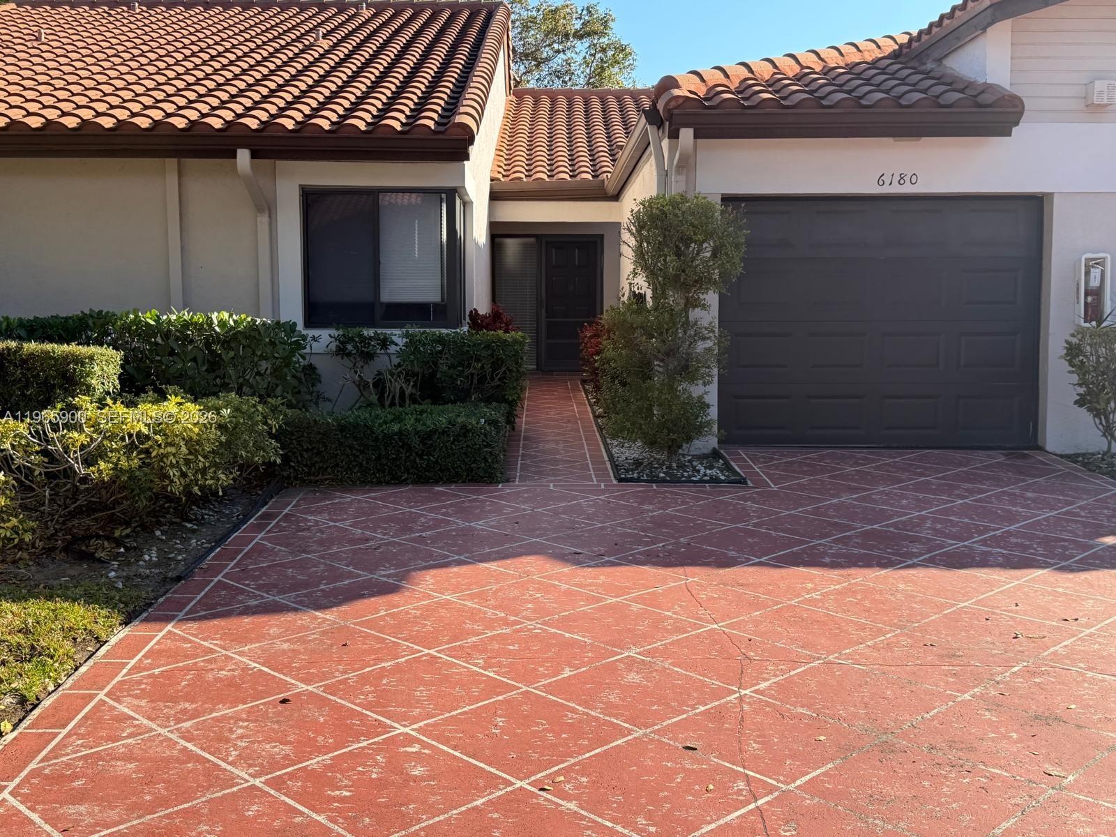 A single-story house features a red tiled roof, a dark garage door, and a patterned driveway — 6180 Kings Gate Cir, Delray Beach FL 33484, DELRAY BEACH, FL