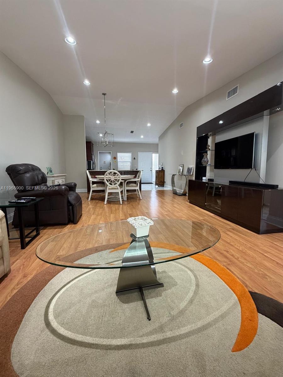 A living room features wood-look flooring, a glass coffee table, and a wall-mounted television — 6180 Kings Gate Cir, Delray Beach FL 33484, DELRAY BEACH, FL