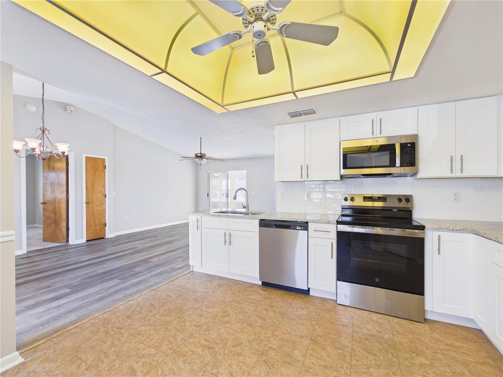 A kitchen with white cabinets, stainless steel appliances, and a yellow tray ceiling with fan — 10482 S CLINT LOOP, FLORAL CITY, FL