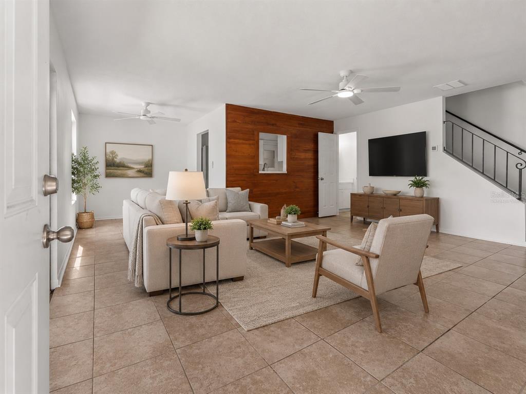 A living room features tile floors, a wood-paneled accent wall, and a staircase — 1016 SPRING MEADOW DRIVE UNIT 12, KISSIMMEE, FL