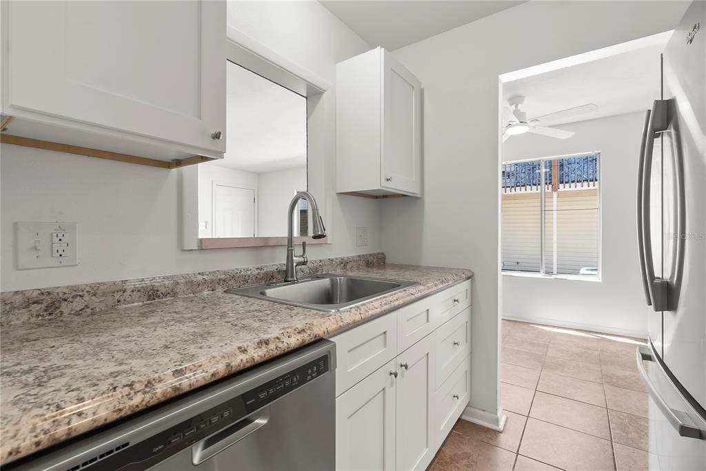 A kitchen features white cabinets, granite countertops, a stainless steel sink, and a dishwasher — 1016 SPRING MEADOW DRIVE UNIT 12, KISSIMMEE, FL
