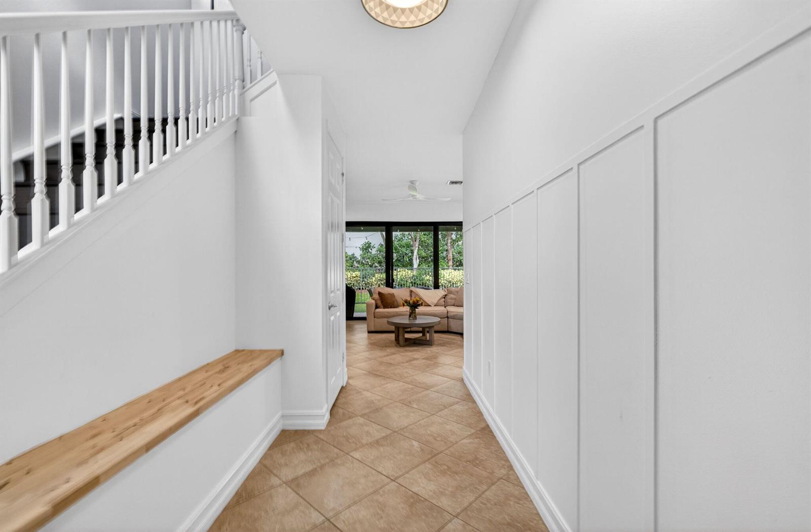 A white hallway features a wooden bench, a staircase, and board-and-batten wall paneling — 13769 Moss Agate Avenue, Delray Beach FL 33446, DELRAY BEACH, FL