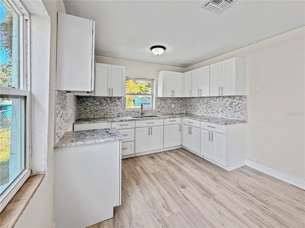 A kitchen features white cabinets, granite countertops, a mosaic tile backsplash, and light wood flooring — 642 20TH STREET, ORLANDO, FL