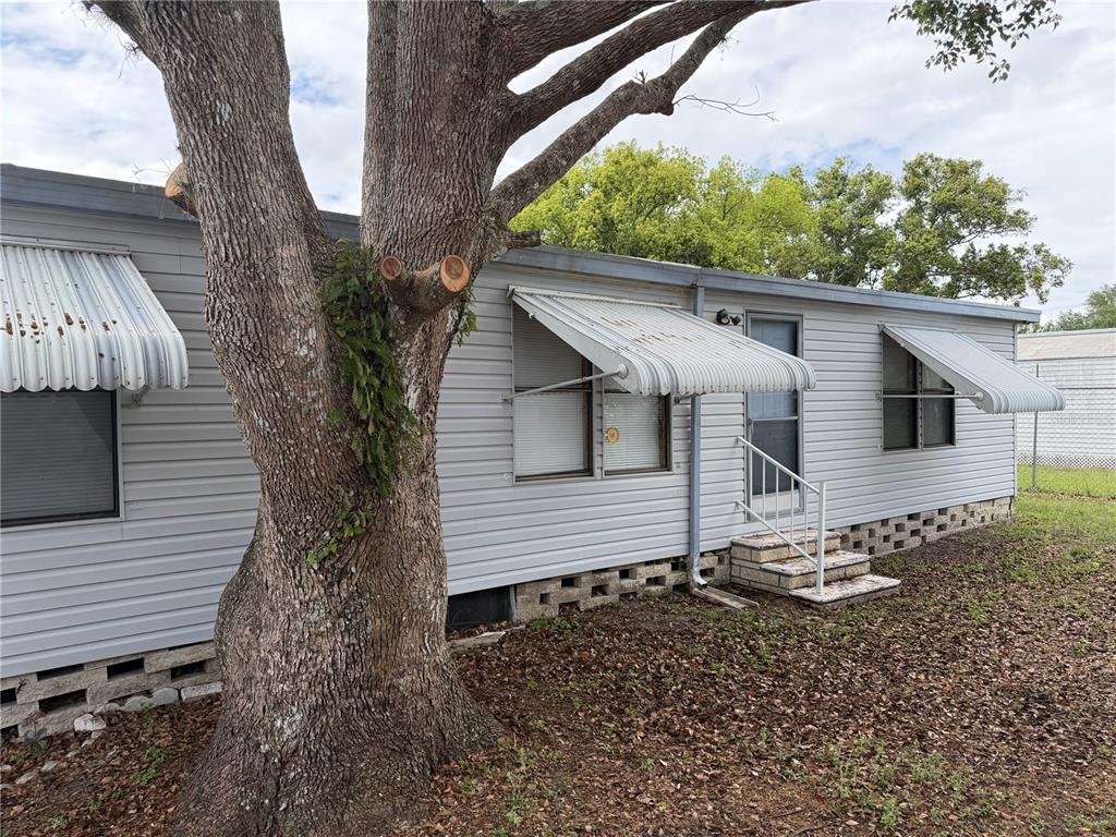 A single-story mobile home with light gray siding, metal window awnings, and a large tree — 34321 COUNTRYSIDE DRIVE, WESLEY CHAPEL, FL
