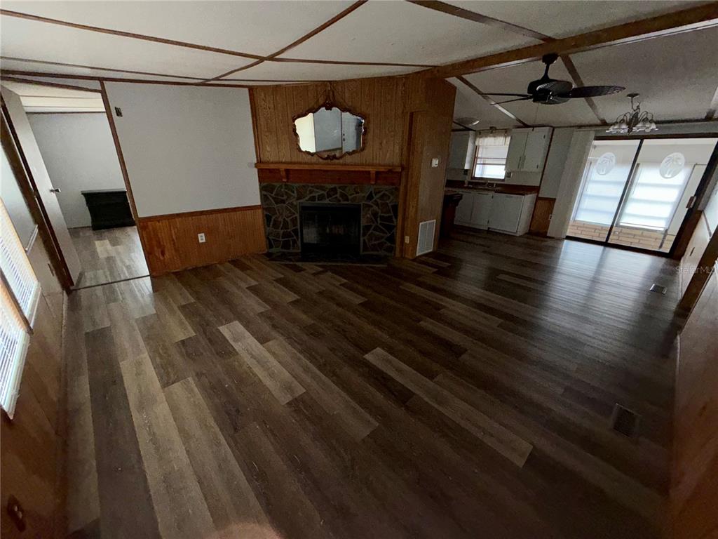 A living room with wood-look flooring, a stone fireplace, and an adjacent kitchen area — 34321 COUNTRYSIDE DRIVE, WESLEY CHAPEL, FL